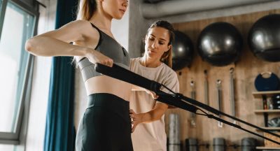 White woman working out on exercise machine during pilates class with coach in gym